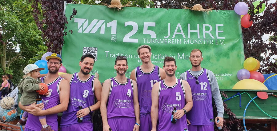 Basketball-Team des TV Münster in lila Trikots vor der Wand „125 Jahre TVM“